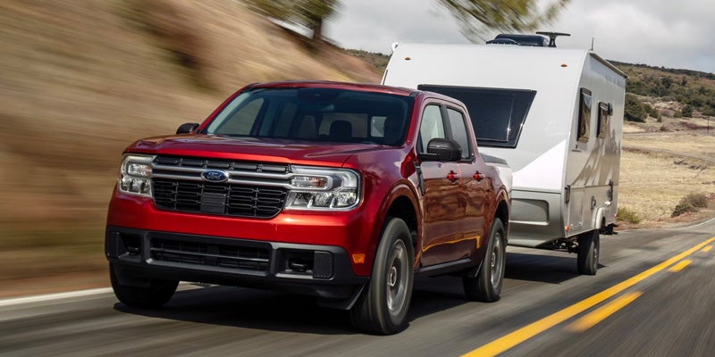 A red truck pulling a trailer on the road.